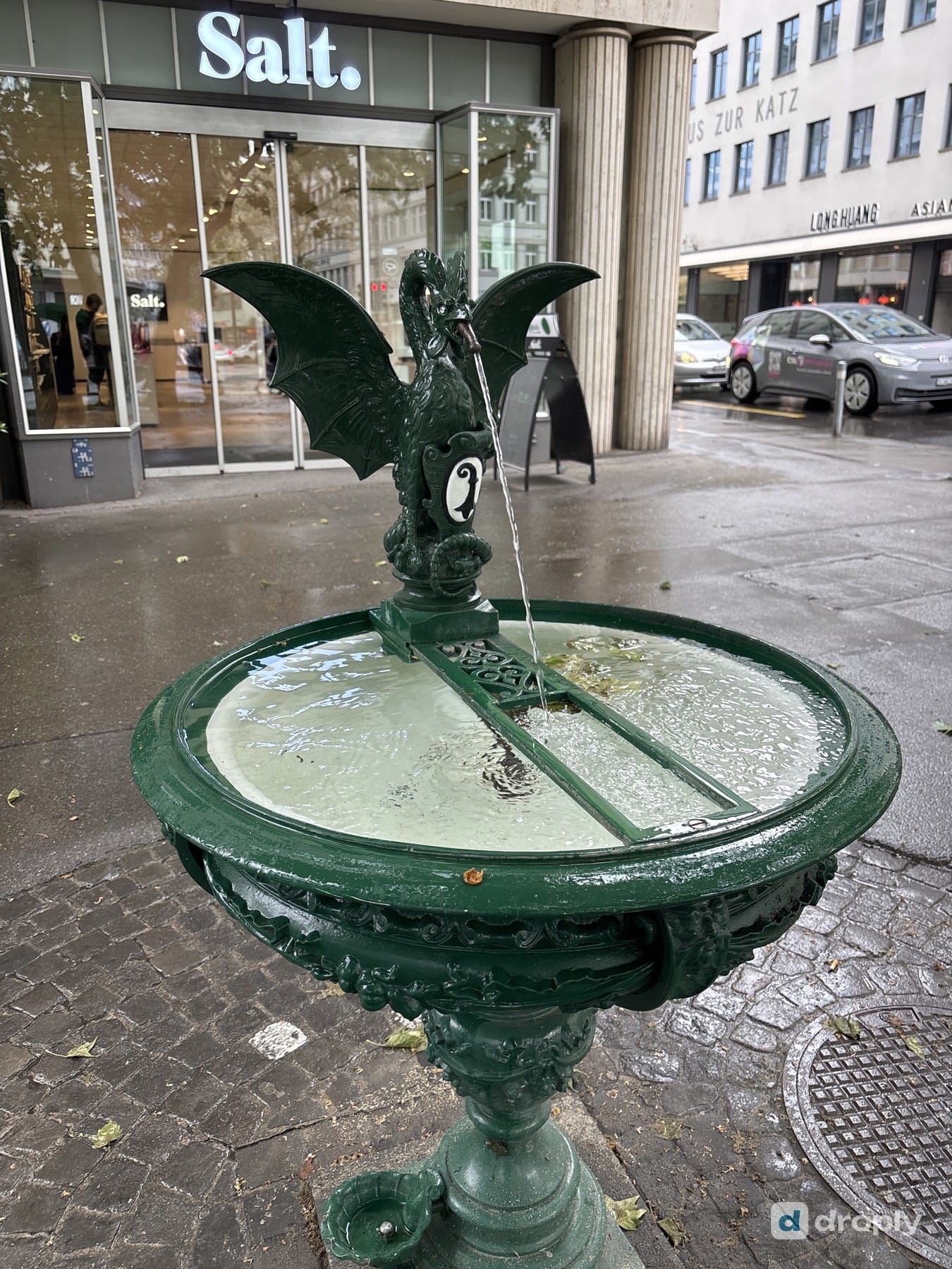 The green Basiliskenbrunnen with a winged dragon in front of a shop in Zurich