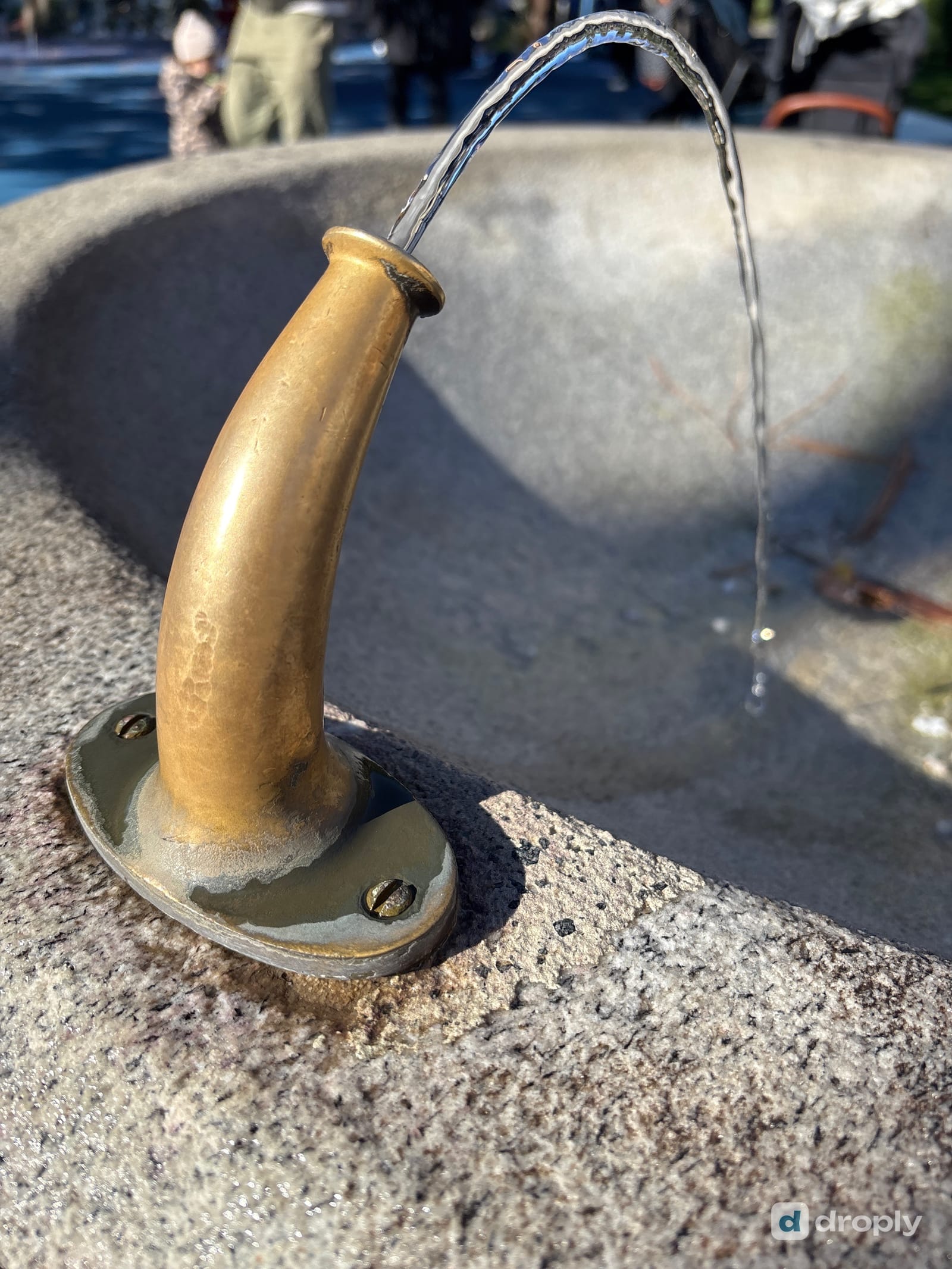 Ein Messingrohr in einem Granitblock, aus dem klares Wasser läuft, in Muralto bei Locarno im Tessin