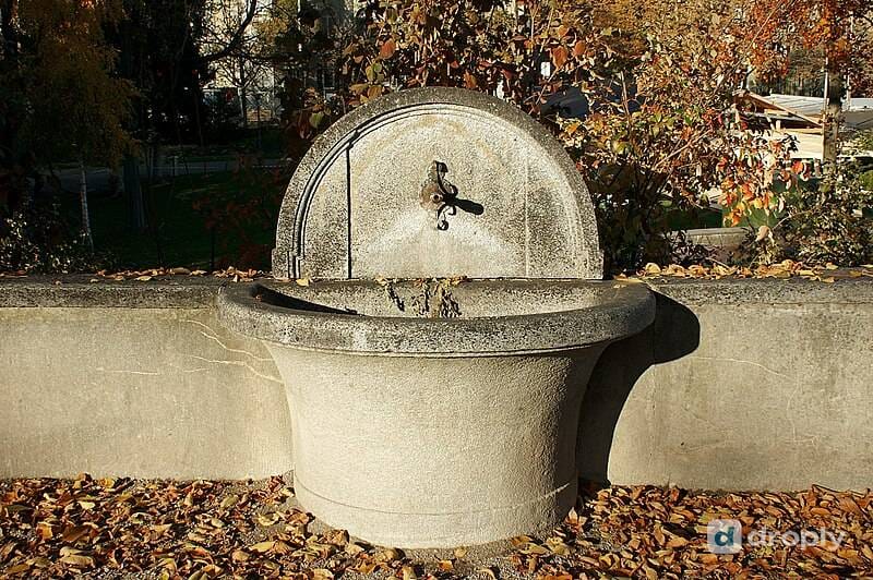 A stone fountain with a spout on the Kleine Schanze in Bern, surrounded by autumn leaves