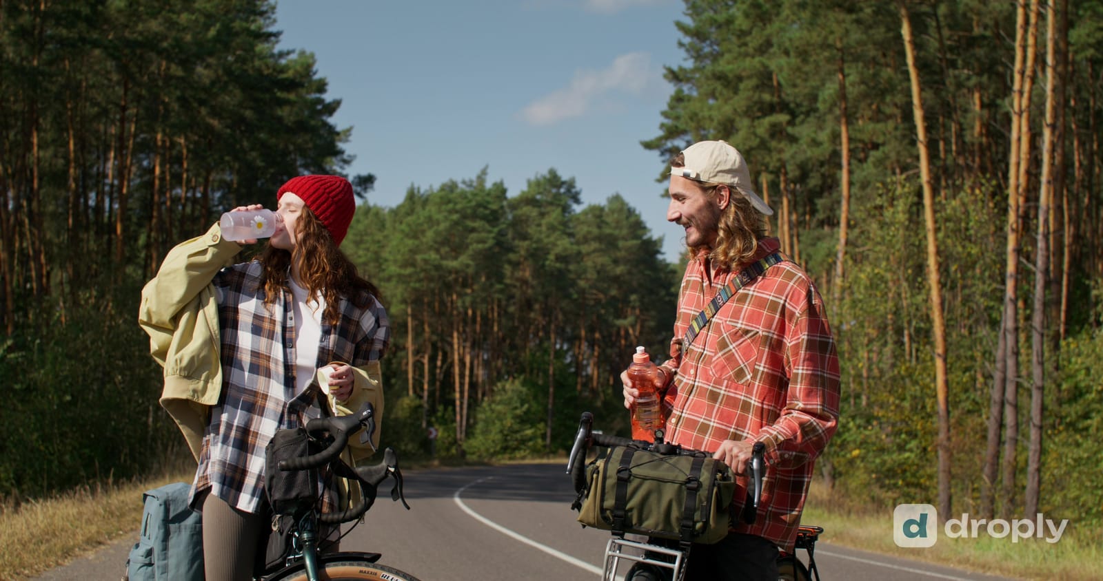Zwei Radfahrende stehen mit ihren Fahrrädern am Rand einer Waldstrasse und trinken aus ihren Flaschen