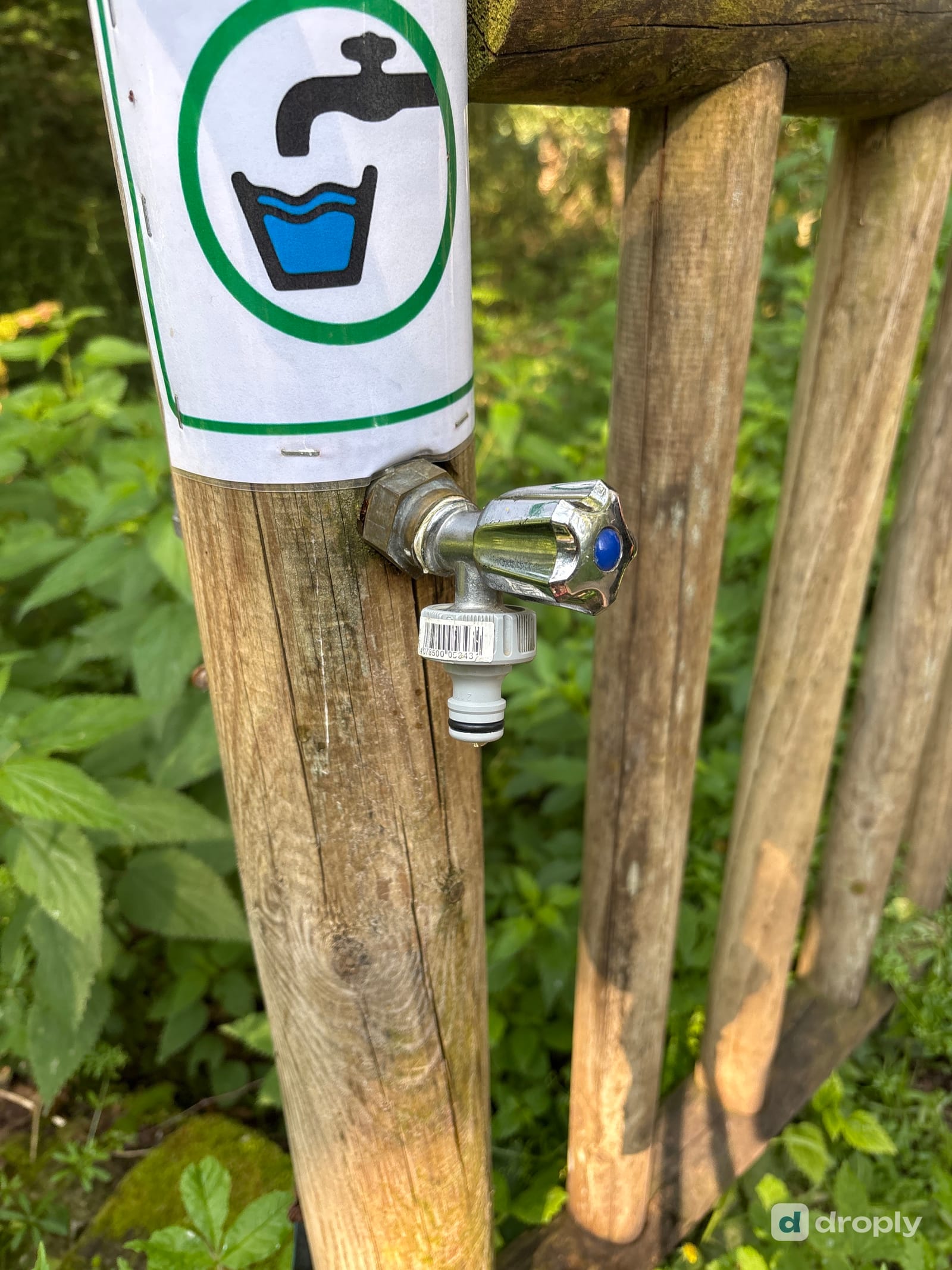 Ein Wasserhahn an einem Holzpfosten mit grünem Trinkwasser-Piktogramm, am Weg bei Golinhac im Aveyron in Frankreich