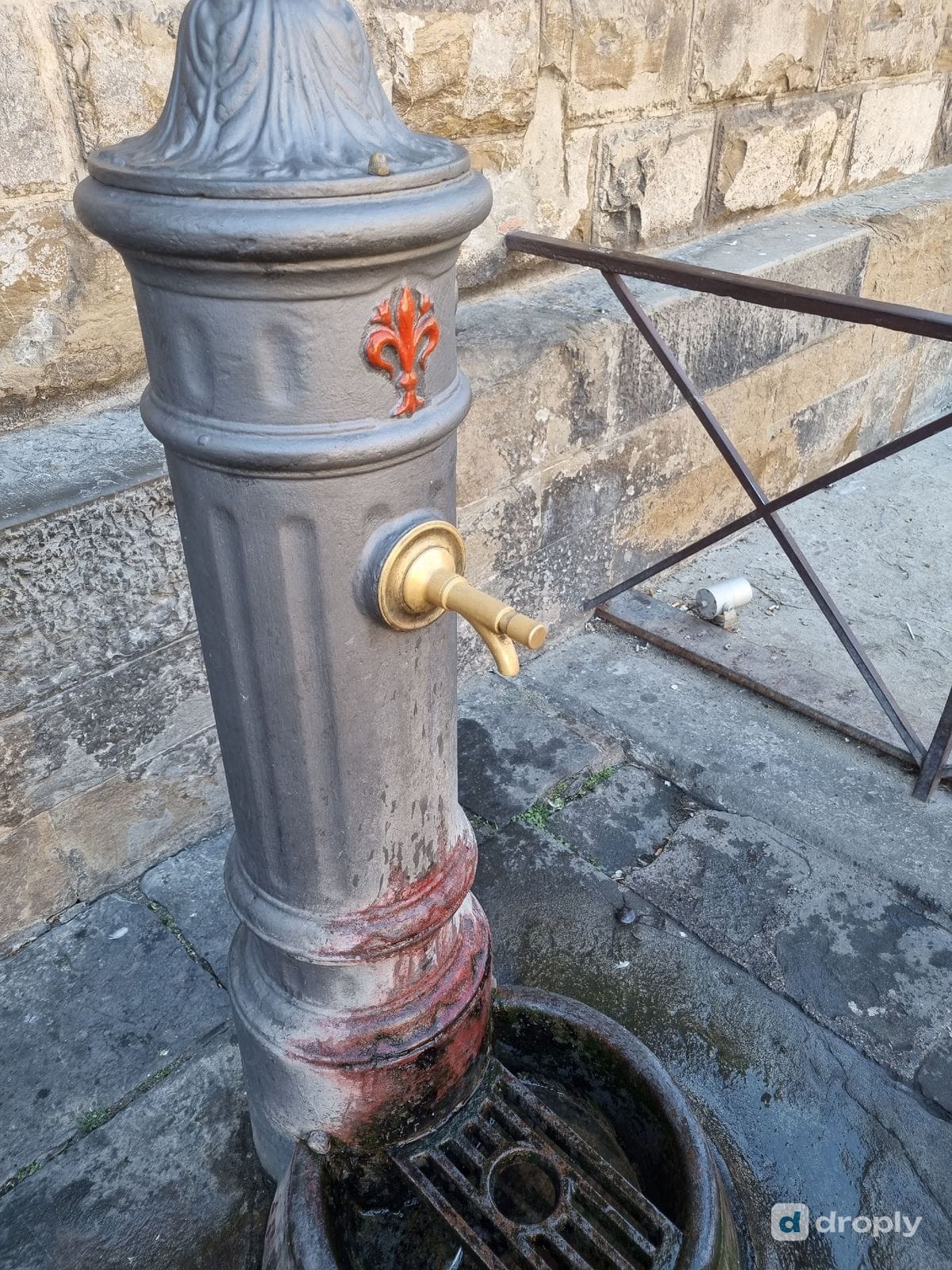 A classic cast-iron drinking fountain in Florence's historic center, marked with a small red Florentine lily emblem