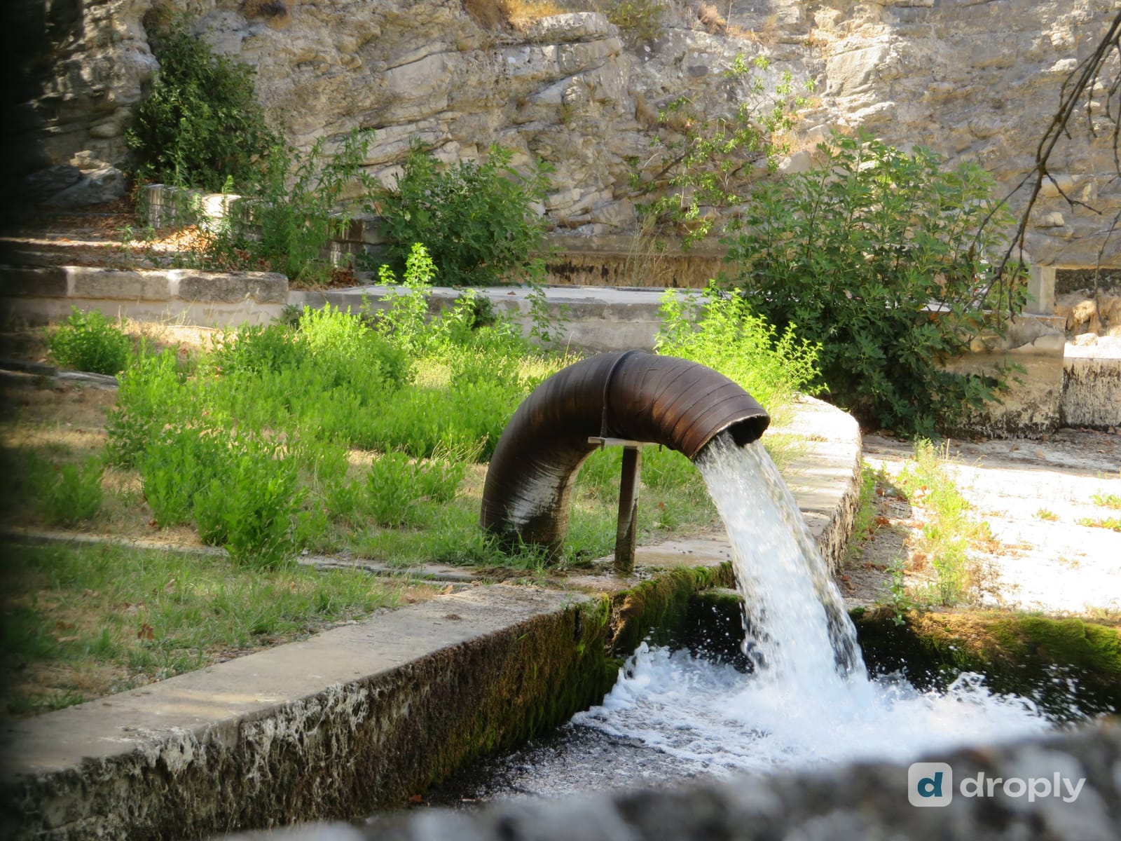 High-volume karst spring near Saint-Clément-de-Rivière in the Hérault, gushing from a pipe into a basin in front of a limestone cliff