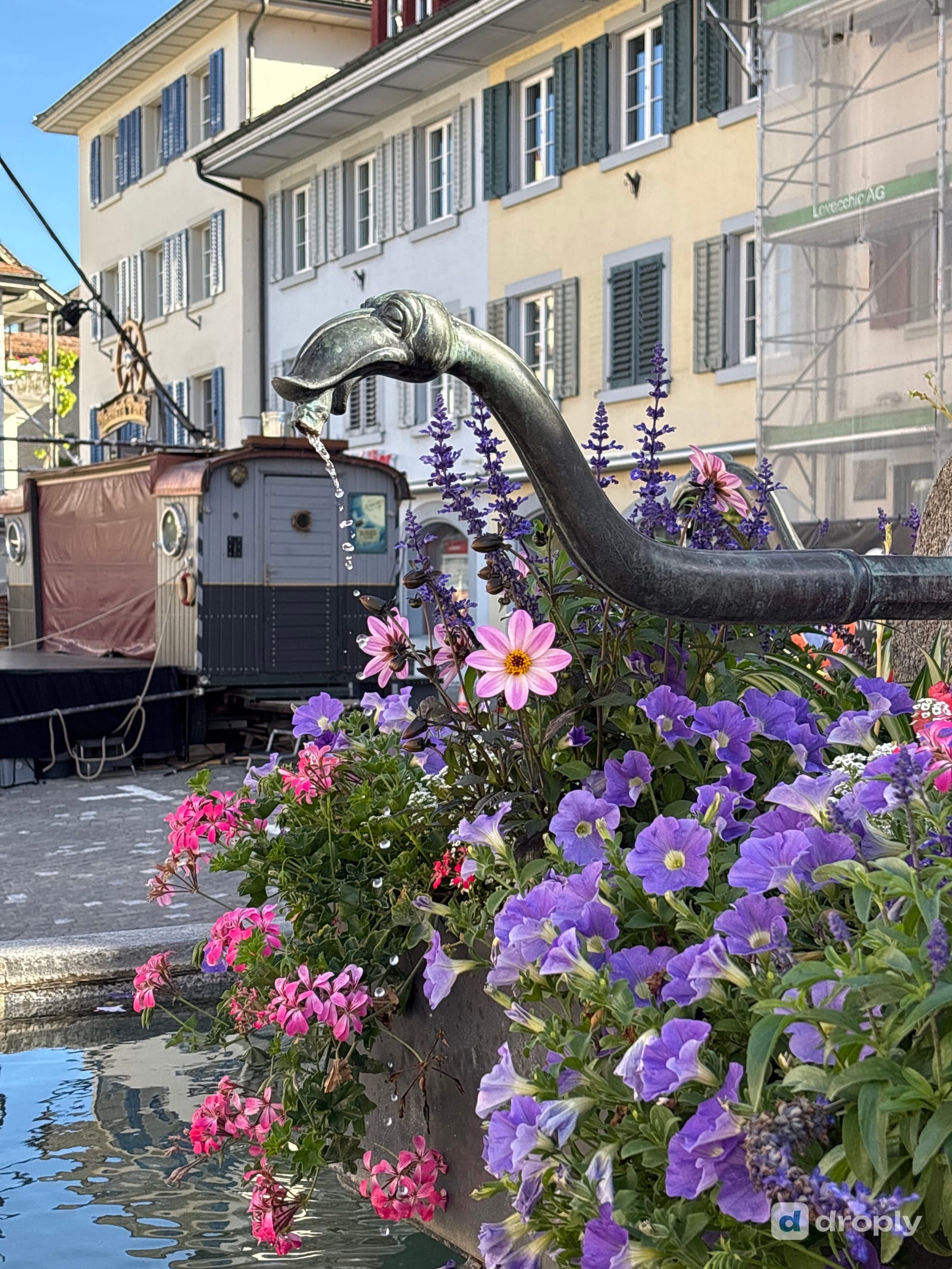 Ein kunstvoll verzierter Bronzebrunnen fliesst zwischen Blumen in der Altstadt von Sursee, Schweiz