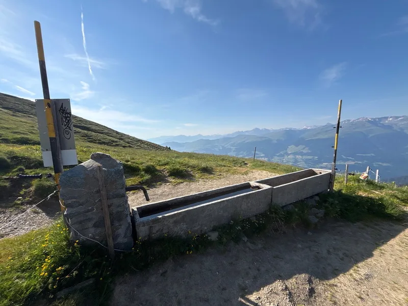 A pair of stone cattle troughs on a high ridge in Graubünden, Switzerland, with a long alpine valley opening up beyond.
